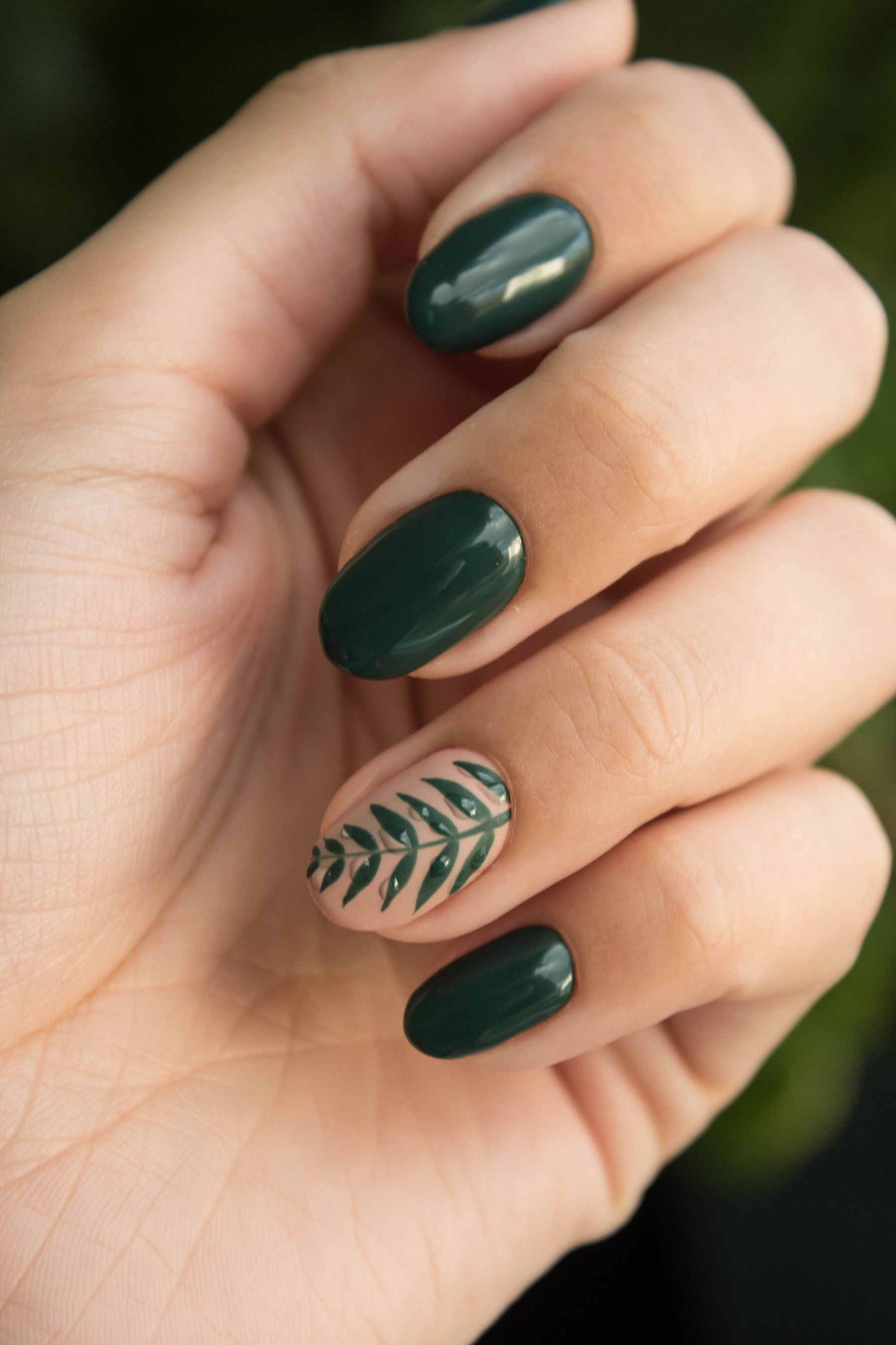 Hand with green nail art and a leaf design